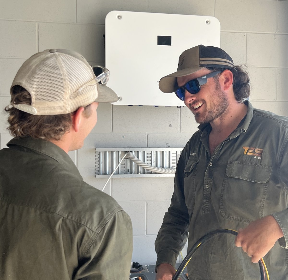 An accredited installer instructs an apprentice during an inverter installation